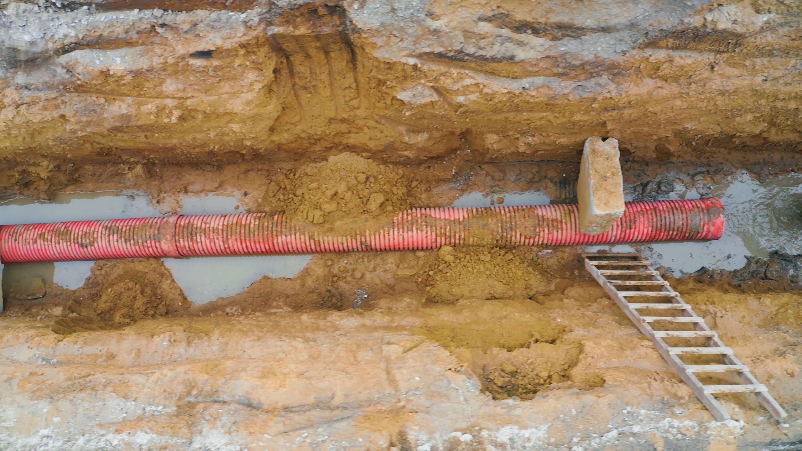 Red corrugated pipe in excavation trench for utility installation