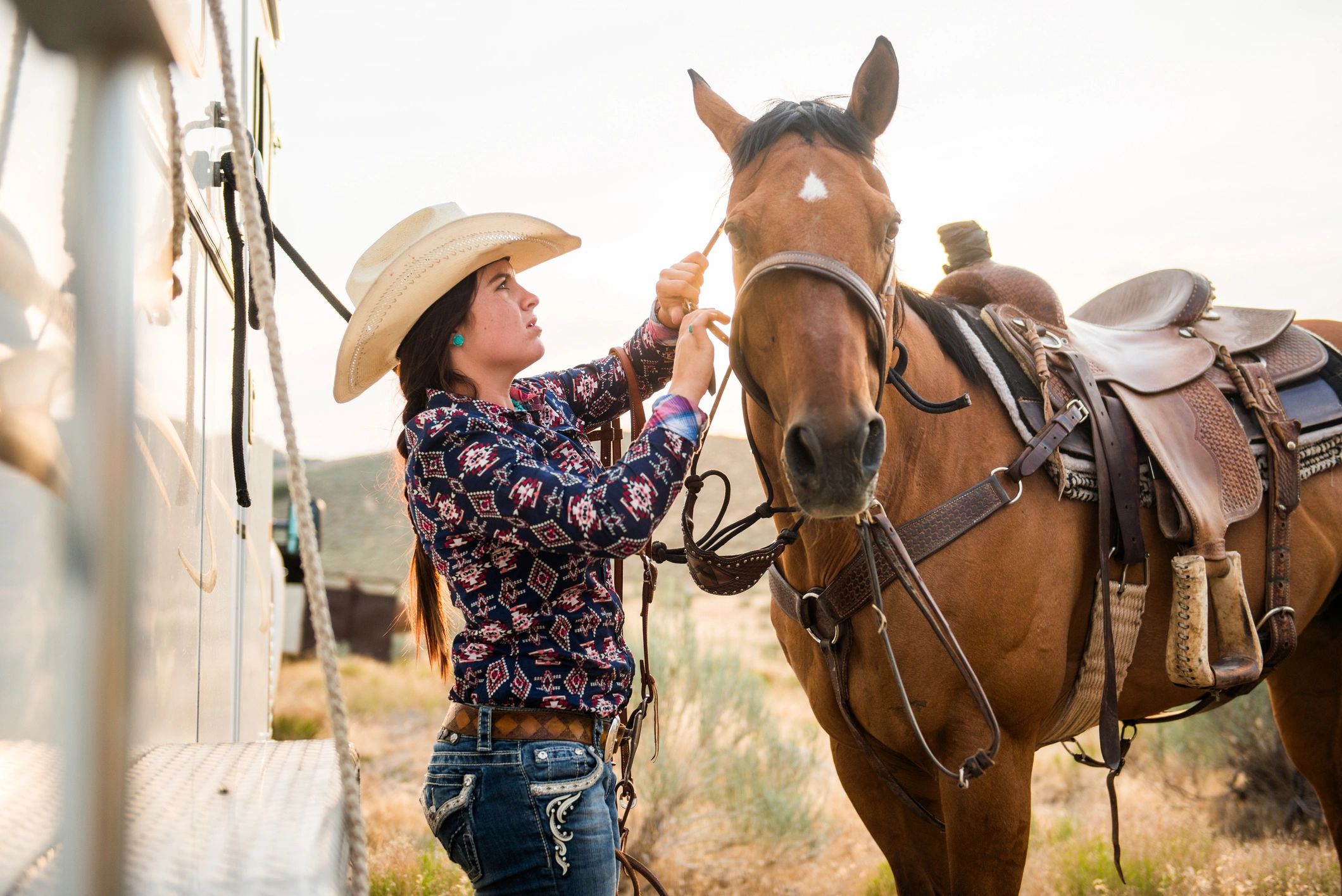 Cowgirl preparing a horse to ride at sunset